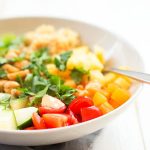This crunchy salad contains bell peppers, cucumbers, cherry tomatoes, pineapple, and quinoa, and is sprinkled with cilantro and peanuts and served in a bowl.