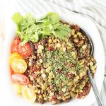 A bowl is filled with lentils and topped with herbs, with halved cherry tomatoes on the side.