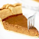 A slice of pumpkin pie with flaky crust is cut into with a fork.