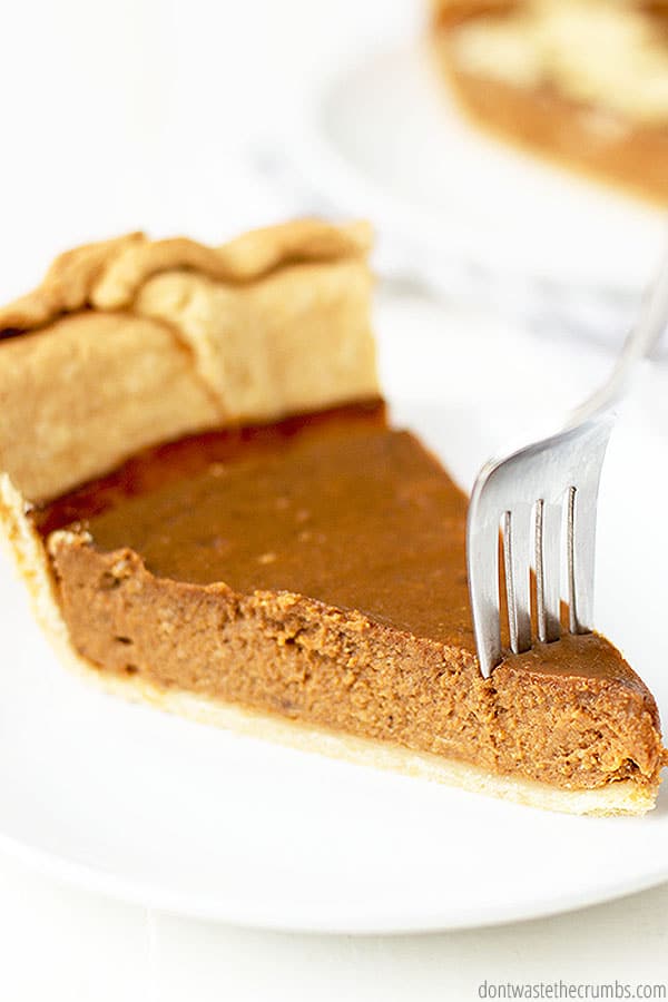 A slice of pumpkin pie with flaky crust is cut into with a fork.