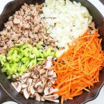 Ground turkey, chopped onion and celery, julienned carrot, and sliced mushrooms sit in a cast iron skillet.