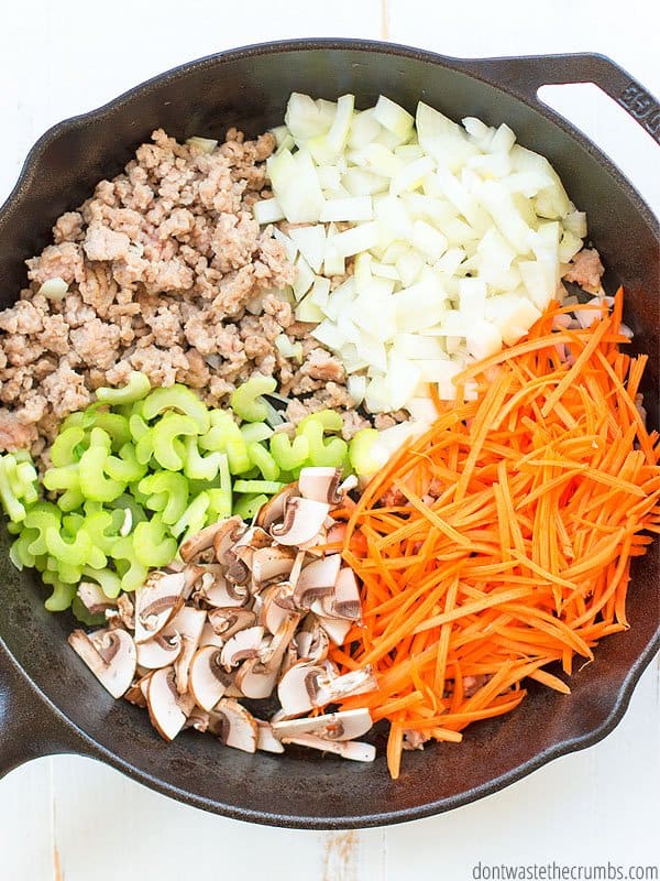 Ground turkey, chopped onion and celery, julienned carrot, and sliced mushrooms sit in a cast iron skillet.